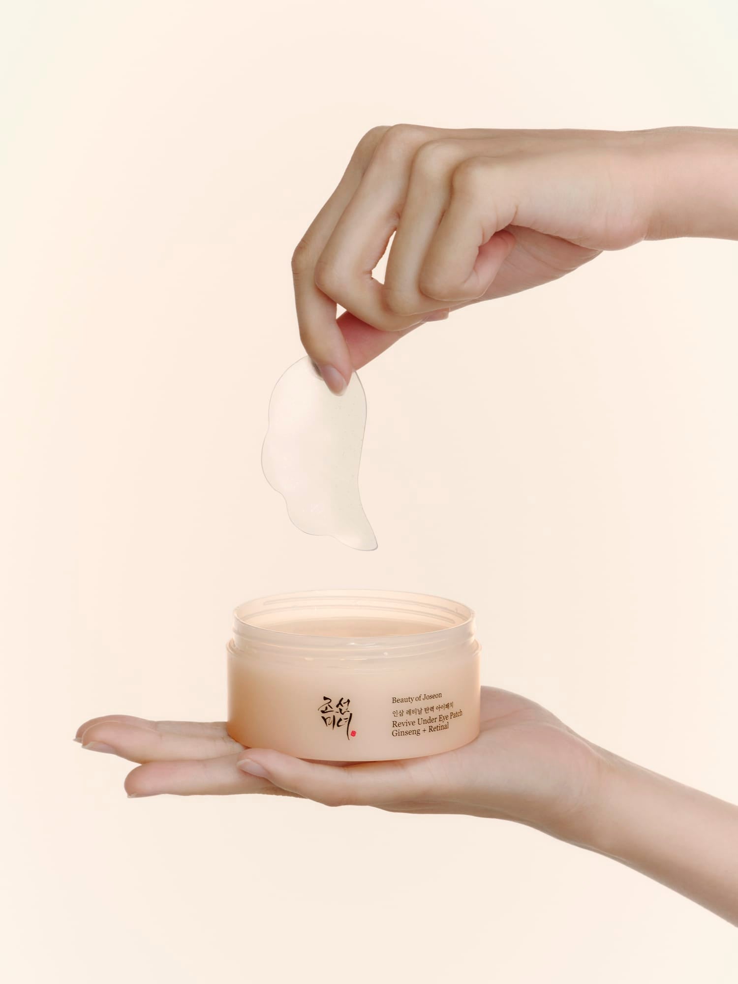 A hand holds an open beige cosmetic jar while another hand lifts a translucent patch of whitening mask above it, against a soft cream background.