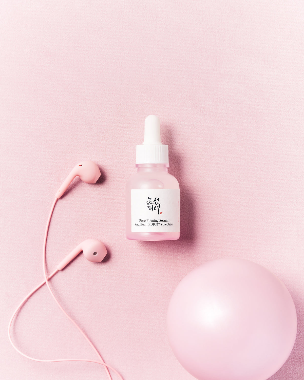 a pink bottle with a white cap next to a pink ball and earphones