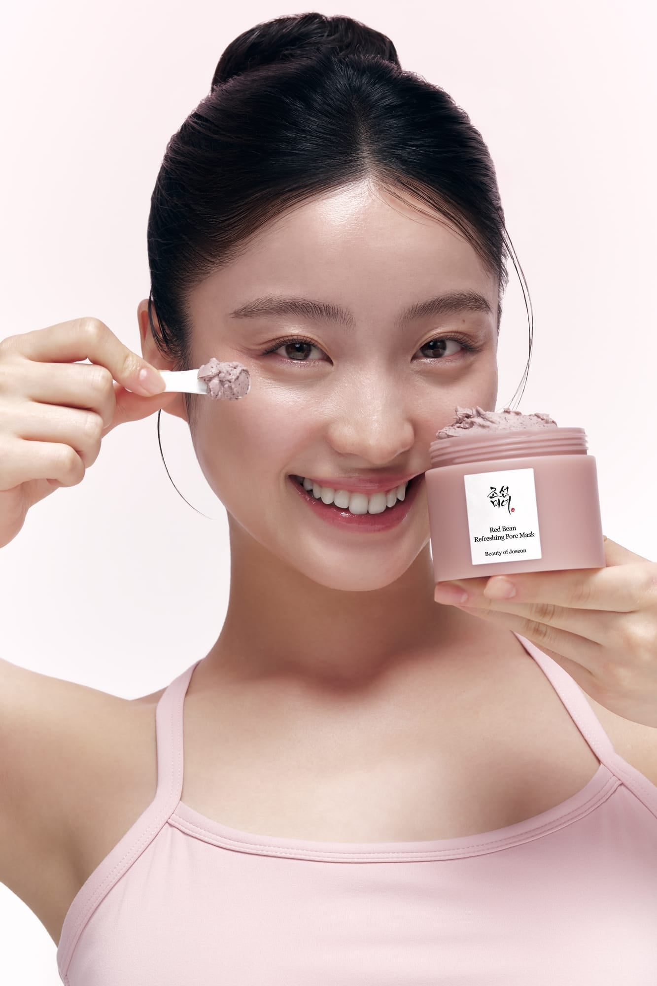 Woman applying cream to her face with a pink jar of cream in front of her.